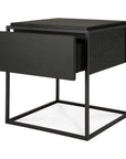 The Monolit Nightstand by Ethnicraft features a modern square design in black oak with an open metal frame and single drawer, highlighting the brand’s signature minimalist style and classic European refinement.