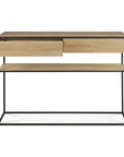 The Monolit Console - Oak by Ethnicraft features a black metal frame, two solid oak drawers (one partially open), a matching lower shelf, and minimalist design with clean, straight lines.