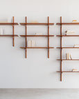The Ethnicraft PI Wall Shelf - Mahogany (5 shelves) displays books neatly and vertically, creating an organized, airy feel against a white wall and concrete floor.