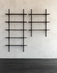 Two sets of Ethnicraft’s Pi Wall Shelf - Dark Mahogany (3 shelves) are mounted in a grid pattern on a light grey textured wall above a dark wooden floor, their minimalist frames empty and striking against the surface.