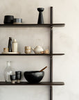 Three Ethnicraft Pi Wall Shelves in dark mahogany display ceramics, glassware, a teapot, cups, bottles, and a bamboo whisk on a light wall. This minimalist decor highlights modern elegance with neutral tones. (Set of 3 shelves).