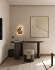 A minimalist home office with the Ethnicraft Boomerang Desk, a round textured stool, abstract wall art, and neutral finishes—showcasing calm elegance and classic European refinement.