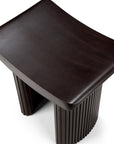 The Roller Max Stool by Ethnicraft features a modern dark mahogany finish, a smoothly curved rectangular seat, and cylindrical legs, shown here against a white background.