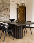 A modern dining area with Ethnicraft's Sequence Dining Table, matching chairs, glass globe pendants, abstract wall art, a geometric wooden door, and a light herringbone floor.