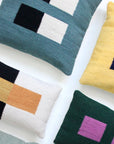 Five handwoven Ania Brzeski pillows, including Pillow 04: Blue + Black, feature geometric color-block patterns in blue, green, yellow, black, white, purple, and orange on a white surface for a striking modernist look.