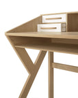 The Origami Desk - Cream by Ethnicraft is a modern European oak desk with an angular design, X-shaped support, two small white drawers with horizontal handles at the back corner, and an open shelf underneath.