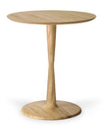 The Ethnicraft Torsion Dining Table - Oak is a small, round table with a single tapered pedestal, circular base, and smooth natural finish that highlights its minimalist modern design inspired by Ethnicraft’s woodworking techniques.