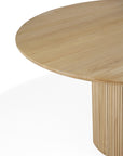The Ethnicraft Roller Max Round Dining Table in oak features a smooth circular top and a slatted cylindrical base, shown against a white background.