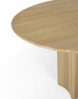 The Roller Max Round Dining Table by Ethnicraft features light solid oak, a smooth top, and a distinctive vertical slatted base, shown here against a white background.