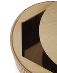 The Ethnicraft Roller Max Coffee Table – Oak features a round solid oak design with a smooth top, ribbed textured sides, and a partially open circular lid that reveals hidden inner storage.