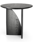 The Geometric Side Table - Black Oak by Ethnicraft features solid oak with a dark finish, a unique base combining a curved panel and cylindrical leg, and visible wood grain for a sleek, minimalist look.