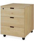 The Ethnicraft Billy Drawer Unit - Oak is a light solid oak three-drawer unit on black wheels, featuring recessed cut-out handles, a lock on the top left of the top drawer, and soft-closing drawers for smooth, quiet operation.