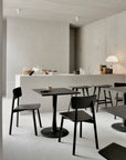 Minimalist café interior with Ethnicraft Osso Barstool - Black, black tables, a white counter with snacks, fruit, coffee makers, glasses, a modern white lamp; featuring neutral concrete walls and soft lighting.