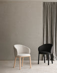 Two modern chairs, including the Ethnicraft Unda Dining Chair, are placed in a minimalist room with a textured gray wall and a gray curtain.