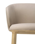 Close-up of the Ethnicraft Unda Dining Chair by Studio Segers, showing its curved light beige upholstered shell and light wooden legs against a white background.