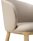A close-up of the Ethnicraft Unda Dining Chair, designed by Studio Segers, showcases its beige upholstered shell, curved backrest, and light wooden legs against a white background.