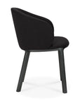 Side view of the Unda Dining Chair by Ethnicraft—a modern black chair with a curved upholstered shell back and seat, plus four sturdy wooden legs. Designed by Studio Segers, it showcases minimalist, contemporary style.