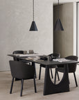 A modern dining area features a black rectangular table, four Ethnicraft Unda Dining Chairs with upholstered shell seats, and two black pendant lights. Books and decor accents rest on the table, set against neutral walls and floors for a minimalist look.