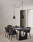 A modern dining room with a black table, six Ethnicraft Unda Dining Chairs featuring sleek upholstered shells, two black pendant lights above, and minimalist decor with black spheres and an open magazine. The walls and carpet are light-colored.