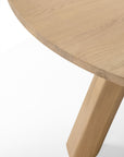 Close-up of a circular solid oak Unda Dining Table by Ethnicraft, featuring a thick, angled leg.