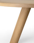 A close-up of the circular solid oak Unda Dining Table by Ethnicraft, showing its tabletop and one thick, cylindrical wooden leg.