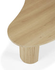 A close-up of Ethnicraft’s Boomerang Coffee Table – Oak, featuring a smooth, organic-shaped top and a cylindrical grooved base in light oak with classic European design, set against a white background.