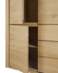 A close-up of the Ethnicraft Shadow Dresser in solid oak showcases its minimalist design, with open doors revealing interior shelves and distinctive horizontal and vertical lines.