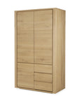 The Ethnicraft Shadow Dresser is a modern solid oak wardrobe with two upper doors and three drawers on the lower right, all in a light natural wood finish.