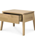 The Ethnicraft Air Nightstand features a minimalist design in a natural light wood finish, with angled legs and a single large drawer partially open to reveal storage, inspired by Ethnicraft furniture style.