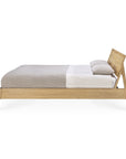 Side view of the Ethnicraft Air Bed, crafted from European oak with an angled headboard, shown neatly made with a light gray blanket, white sheet, and two pillows.