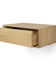 The Ethnicraft Nordic II Hanging Bedside Table is a minimalist, wall-mounted drawer crafted from solid European oak in a light natural finish, shown partially open against a plain white background.