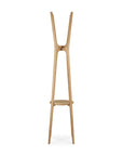 The Ethnicraft PI Coat Stand - Oak is a modern, minimalist solid oak coat stand with three tall, angled legs and a compact central shelf, shown standing upright against a white background.