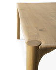 Close-up of the Ethnicraft PI Dining Table - Oak, featuring a smooth, rounded corner, visible oak grain, and sturdy cylindrical legs, set against a plain white background.
