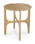 The Ethnicraft Pi Side Table - Oak is a small, round table with a solid oak top featuring gentle edge indents and three legs with curved, intersecting supports in a smooth, minimalist design.