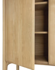 Close-up of the Ethnicraft PI Cupboard - Oak, handcrafted with smooth, rounded edges and a natural wood grain finish. A partially open door reveals three interior shelves in this solid oak storage piece.
