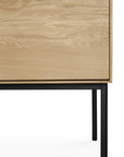 A close-up of the Ethnicraft Whitebird Sideboard - 3 door reveals natural oak grain, sleek black metal legs, and a minimal modern design.