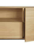 A close-up of Ethnicrafts Whitebird TV Cupboard, featuring a partially open door that reveals an interior shelf. Its minimal, modern design showcases smooth surfaces and the natural solid oak grain.