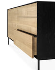 The Ethnicraft Blackbird Sideboard features 2 doors and 3 drawers, crafted in European oak with a black frame and legs for a modern look. One lower drawer is partially open, showcasing the natural wood finish inside.
