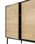 The Ethnicraft Blackbird Sideboard features 2 doors, 3 drawers, a European oak build with a natural finish, and black metal legs. Partially open, one door reveals spacious shelves within this modern cabinet from the Blackbird Collection.