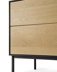The Ethnicraft Blackbird TV Cupboard, part of the Blackbird Collection, is crafted in European oak with a light wood finish, black metal legs, and two large drawers. Shown from an angled side view against a white background.
