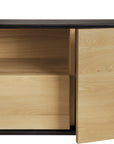 A close-up of the Ethnicraft Blackbird TV Cupboard features light European oak doors—one partially open to reveal an interior drawer. The minimalist cupboard showcases a contrasting dark wood frame.