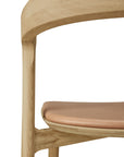 Close-up of the Ethnicraft Bok Dining Chair - Oak with Sienna Leather, highlighting its smooth solid oak frame and sienna leather seat cushion against a plain white background.