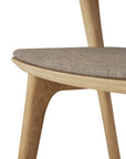 Close-up of Ethnicrafts Bok Dining Chair in oak with warm grey fabric, highlighting its curved solid oak seat, smooth natural wood grain, minimalist design, and upholstered cushion.