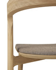 Close-up of the Ethnicraft Bok Dining Chair - Oak with Warm Grey Fabric, highlighting its curved solid oak backrest and cushioned seat, set against a white background.