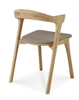 The Ethnicraft Bok Dining Chair in Oak with Warm Grey Fabric features a curved backrest, angled solid oak legs, and an upholstered seat cushion, shown from behind and at an angle.