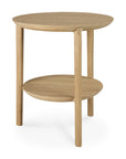 The Ethnicraft Bok Side Table - Oak features a round, solid oak tabletop and lower shelf in a natural light finish, supported by three legs. Its simple, modern design captures Ethnicrafts timeless aesthetic.