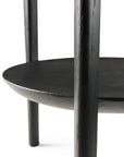 Close-up of the lower half of the Ethnicraft Bok Side Table - Black, featuring black solid oak with visible grain, a round shelf, three cylindrical legs, and a smooth finish.