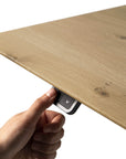 A hand presses the downward arrow button below an oak tabletop, adjusting the height of the Ethnicraft Bok Adjustable Desk for ergonomic comfort.