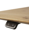Close-up of the Ethnicraft Bok Adjustable Desk - Oak’s motorised control panel with up and down arrow buttons, mounted under the light oak tabletop for easy desk height adjustment.