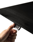 A hand presses a downward arrow button on the underside of the sleek, black Bok Adjustable Desk by Ethnicraft, adjusting its height.